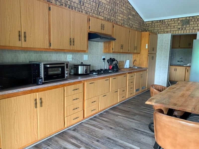 A functional kitchen featuring wood-look cabinetry, a gas hob with extractor fan, and a tiled backsplash, with an adjacent scullery area.