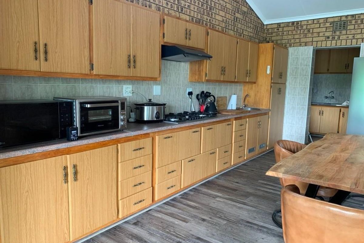 A functional kitchen featuring wood-look cabinetry, a gas hob with extractor fan, and a tiled backsplash, with an adjacent scullery area.