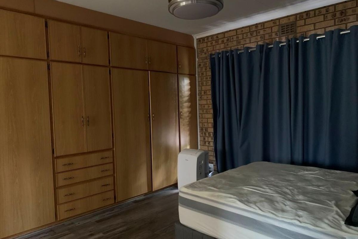 Bedroom featuring extensive built-in wooden cabinetry, a textured face-brick feature wall, and modern wood-look flooring.