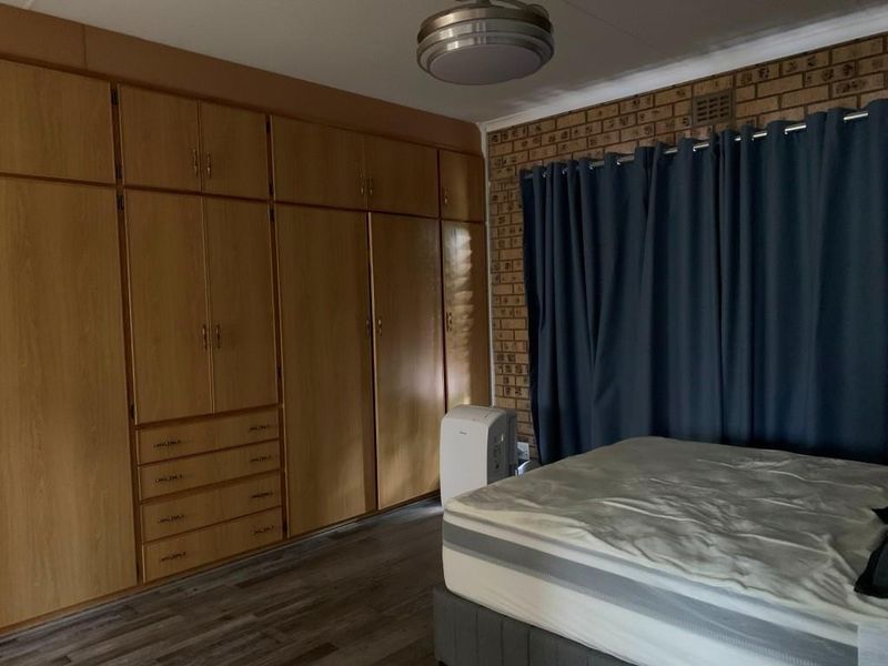 Bedroom featuring extensive built-in wooden cabinetry, a textured face-brick feature wall, and modern wood-look flooring.