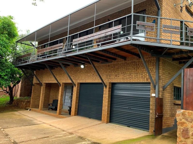 Exterior view of a multi-level brick house featuring a large elevated balcony, double garage, and covered ground-level patio area.
