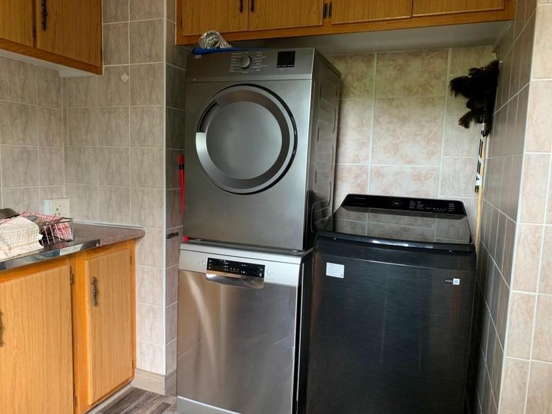 A functional laundry area featuring tiled walls, built-in wooden cabinetry, and space for multiple appliances.