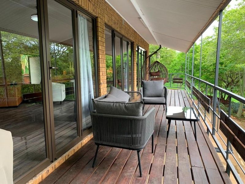 A covered outdoor balcony featuring timber decking, metal railings, and large glass sliding doors providing access to the interior living space.