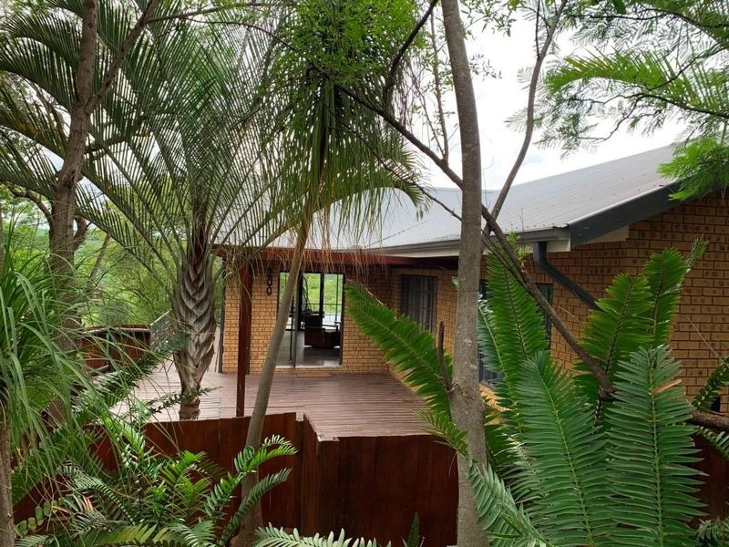 A view of the rear exterior featuring a timber deck, brick facade, and metal roof, surrounded by established garden foliage.