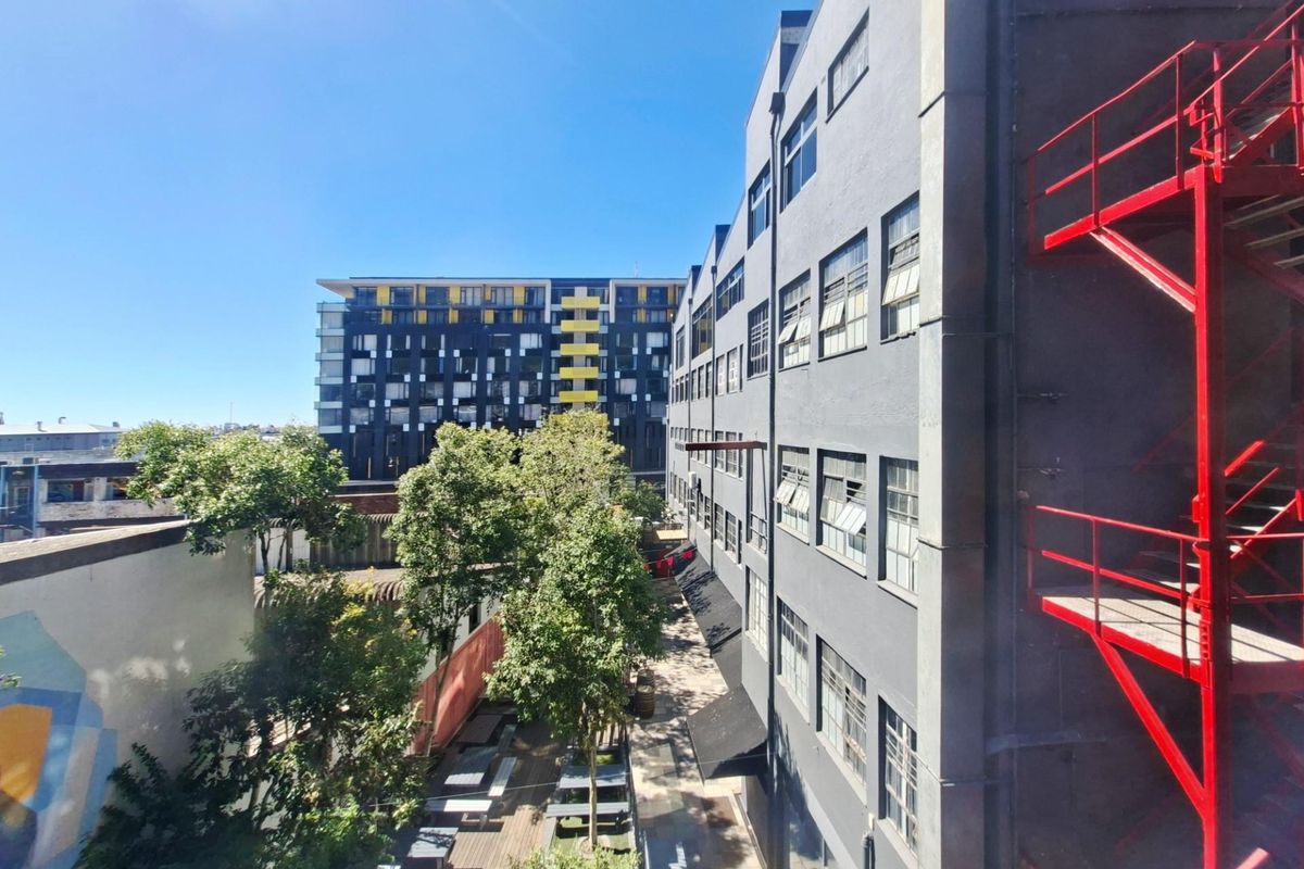 An elevated view of the office building exterior, featuring a prominent red metal fire escape staircase and a landscaped courtyard area below.