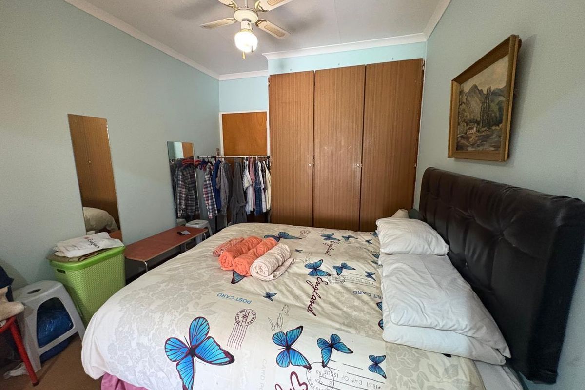 A bedroom featuring built-in wooden wardrobes, a ceiling fan, and light-colored walls, providing a functional and comfortable sleeping space.