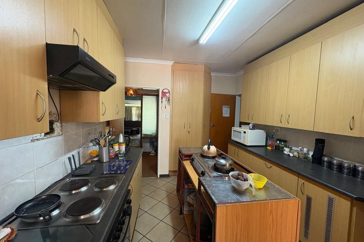 Functional kitchen featuring light wood cabinetry, dark laminate countertops, built-in electric hob, extractor fan, and tiled flooring.