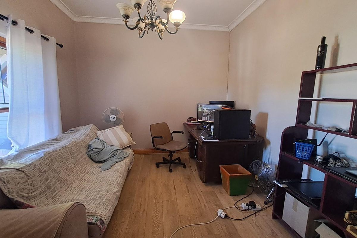 A functional bedroom or home office space featuring laminate wood flooring, crown molding, and a large window with security bars.