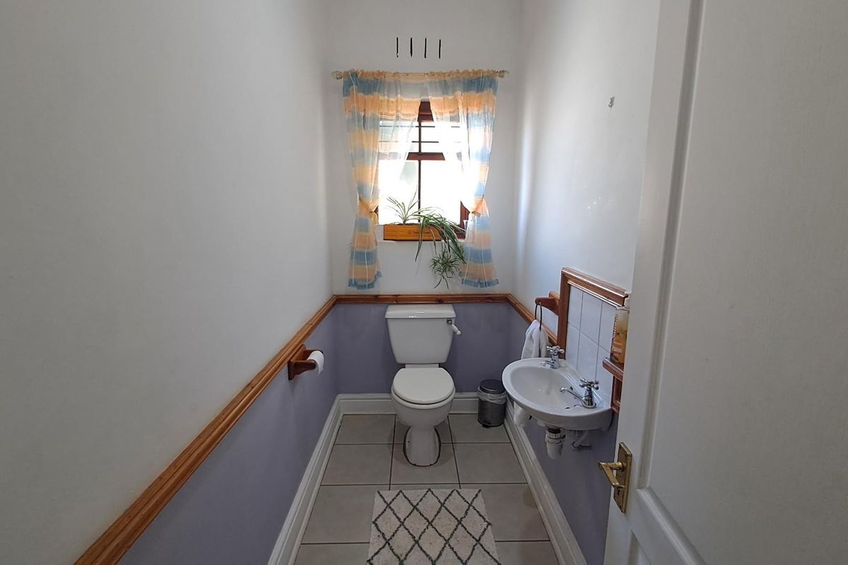 A compact guest cloakroom featuring a wall-mounted basin, a standard toilet, and tiled flooring with decorative dado rail trim.