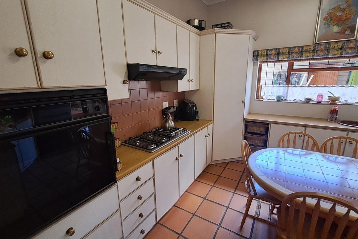 A functional kitchen featuring white cabinetry, a built-in oven, gas hob, extractor fan, and terracotta tile flooring with an integrated dining area.
