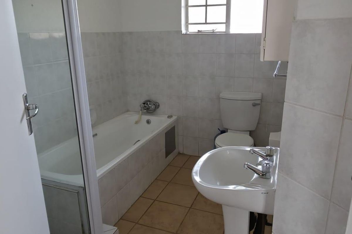 A functional bathroom featuring a bathtub, separate shower enclosure, pedestal basin, and toilet with neutral wall tiling and tiled flooring.