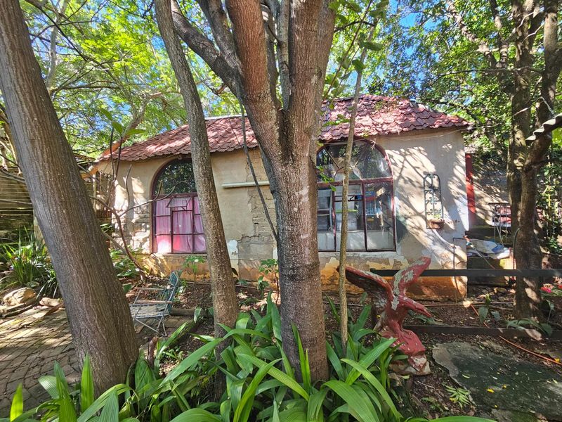 A view of the rear exterior of the property, featuring arched windows, a tiled roof, and mature garden surroundings.