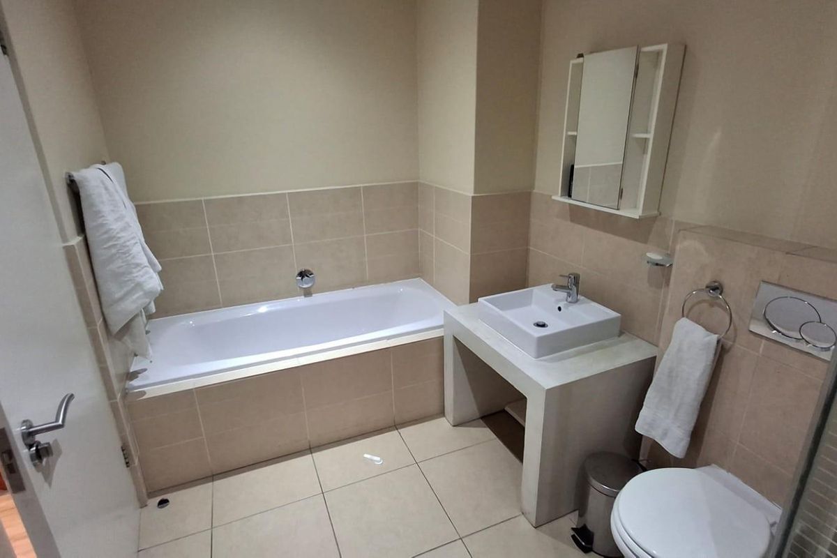 A functional bathroom featuring a built-in bathtub, a modern square basin on a concrete-style vanity, and a wall-mounted toilet.