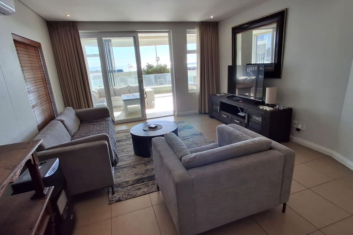A comfortable living room featuring tiled flooring, large sliding glass doors leading to a balcony, and a wall-mounted air conditioning unit.