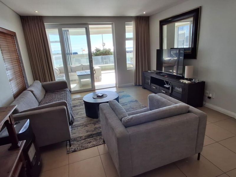 A comfortable living room featuring tiled flooring, large sliding glass doors leading to a balcony, and a wall-mounted air conditioning unit.