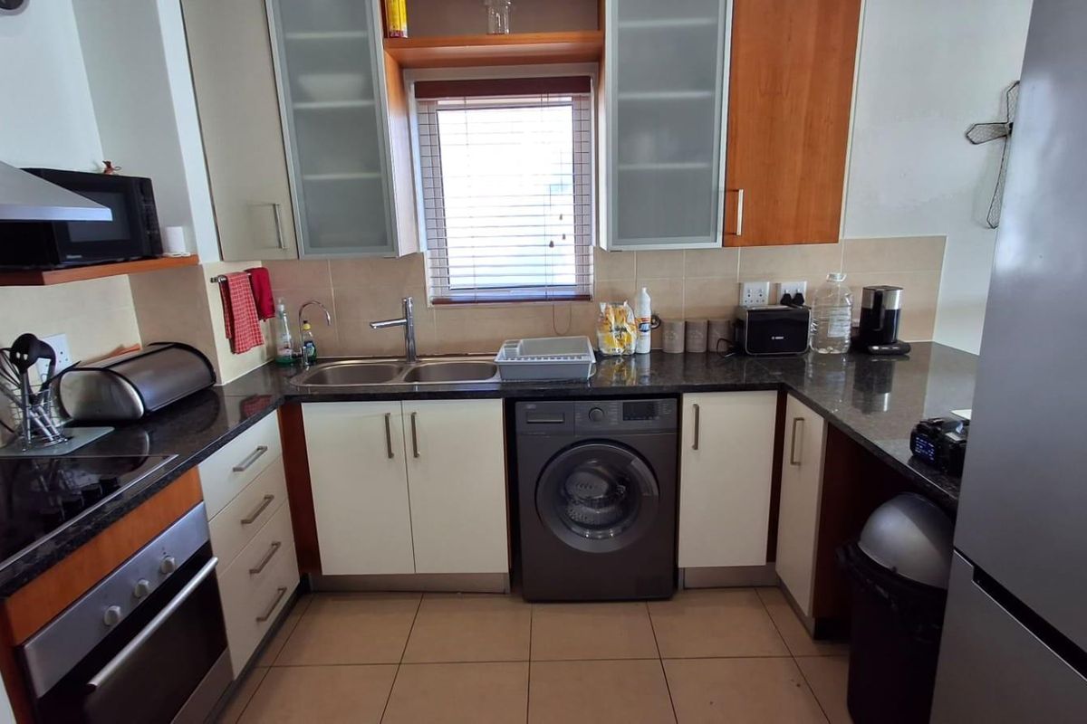 A functional kitchen featuring granite countertops, built-in oven, hob, extractor fan, and integrated laundry appliance space with ample cabinetry.