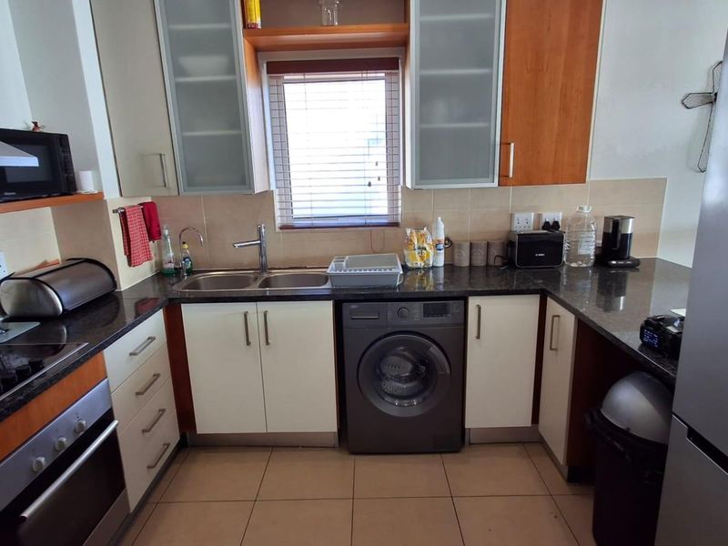 A functional kitchen featuring granite countertops, built-in oven, hob, extractor fan, and integrated laundry appliance space with ample cabinetry.
