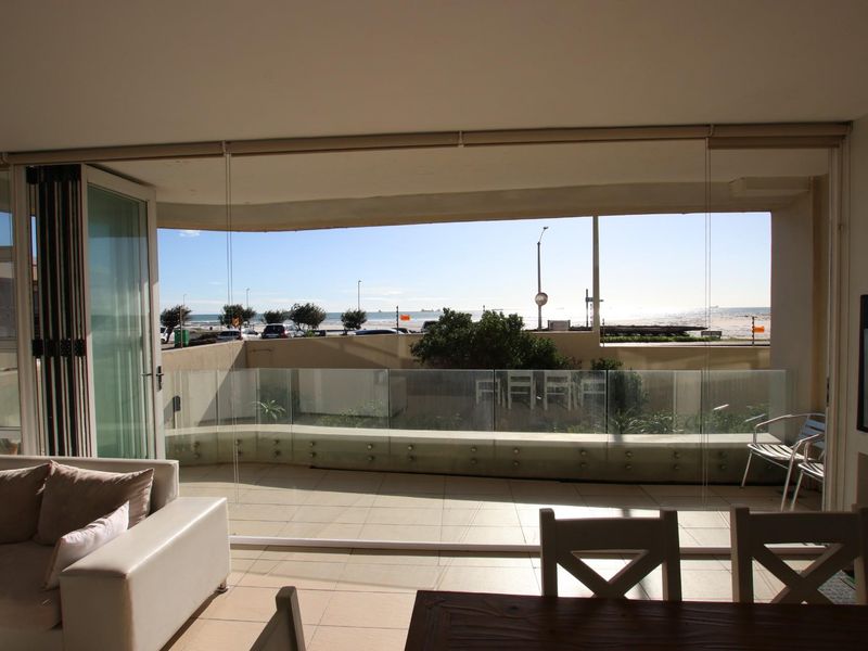 Spacious open-plan living area featuring large glass sliding doors that open onto a private balcony with scenic coastal views.