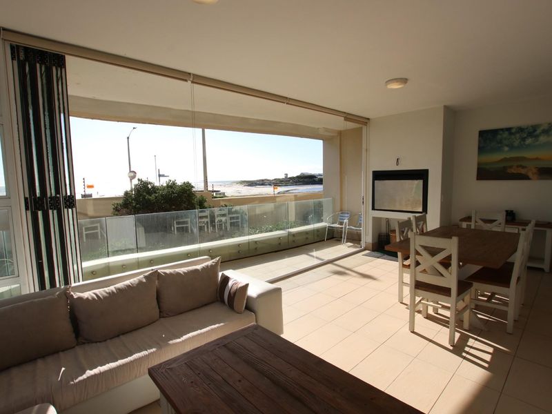 Spacious open-plan living and dining area featuring a built-in fireplace and large glass sliding doors opening onto a balcony with coastal views.
