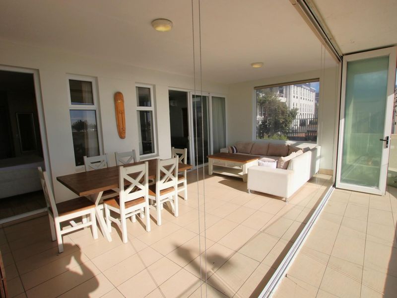 A spacious enclosed balcony featuring tiled flooring, large glass sliding doors, and ample natural light, suitable for dining and relaxation.
