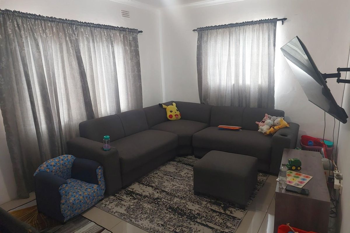 A functional living room featuring tiled flooring, dual window treatments, and a wall-mounted television bracket.