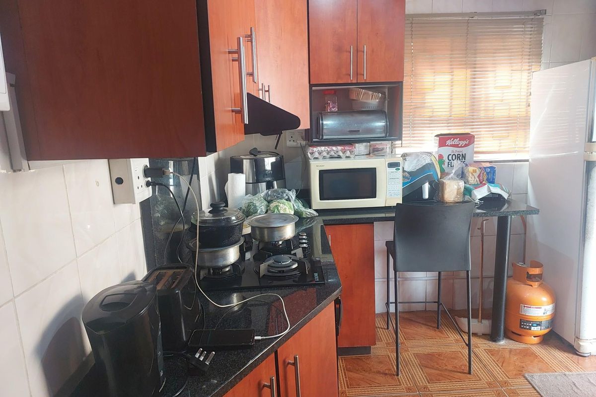 A functional kitchen featuring wood-finish cabinetry, granite countertops, a gas hob, and tiled flooring, offering a practical layout for daily meal preparation.