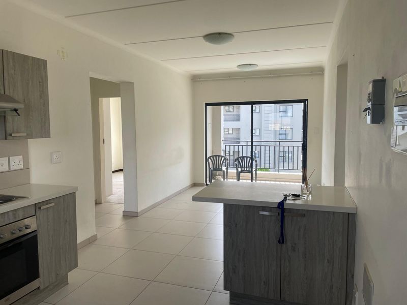 Open-plan kitchen and living area featuring modern grey cabinetry, built-in oven, hob, and tiled flooring, leading to a balcony with sliding glass doors.