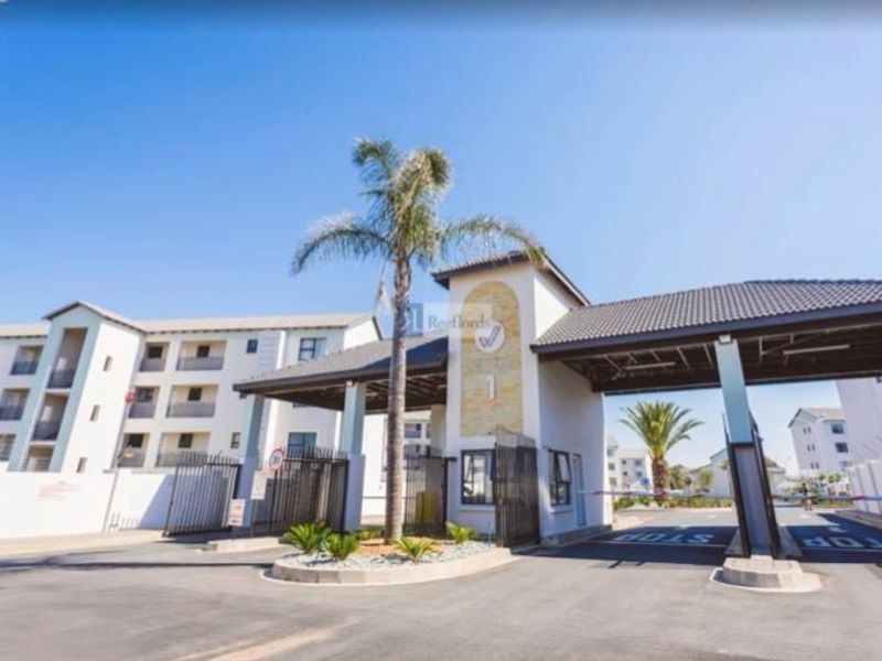 The secure entrance gatehouse of the apartment complex, featuring a paved driveway, boom gate access, and modern architectural design.