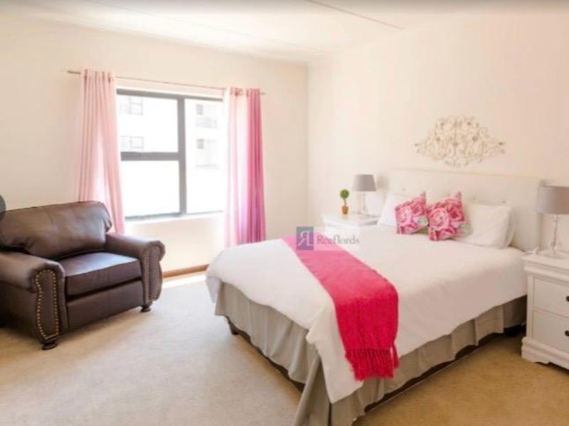 A well-lit bedroom featuring neutral carpeting, a large window with curtain rods, and a spacious layout suitable for a double or queen-sized bed.