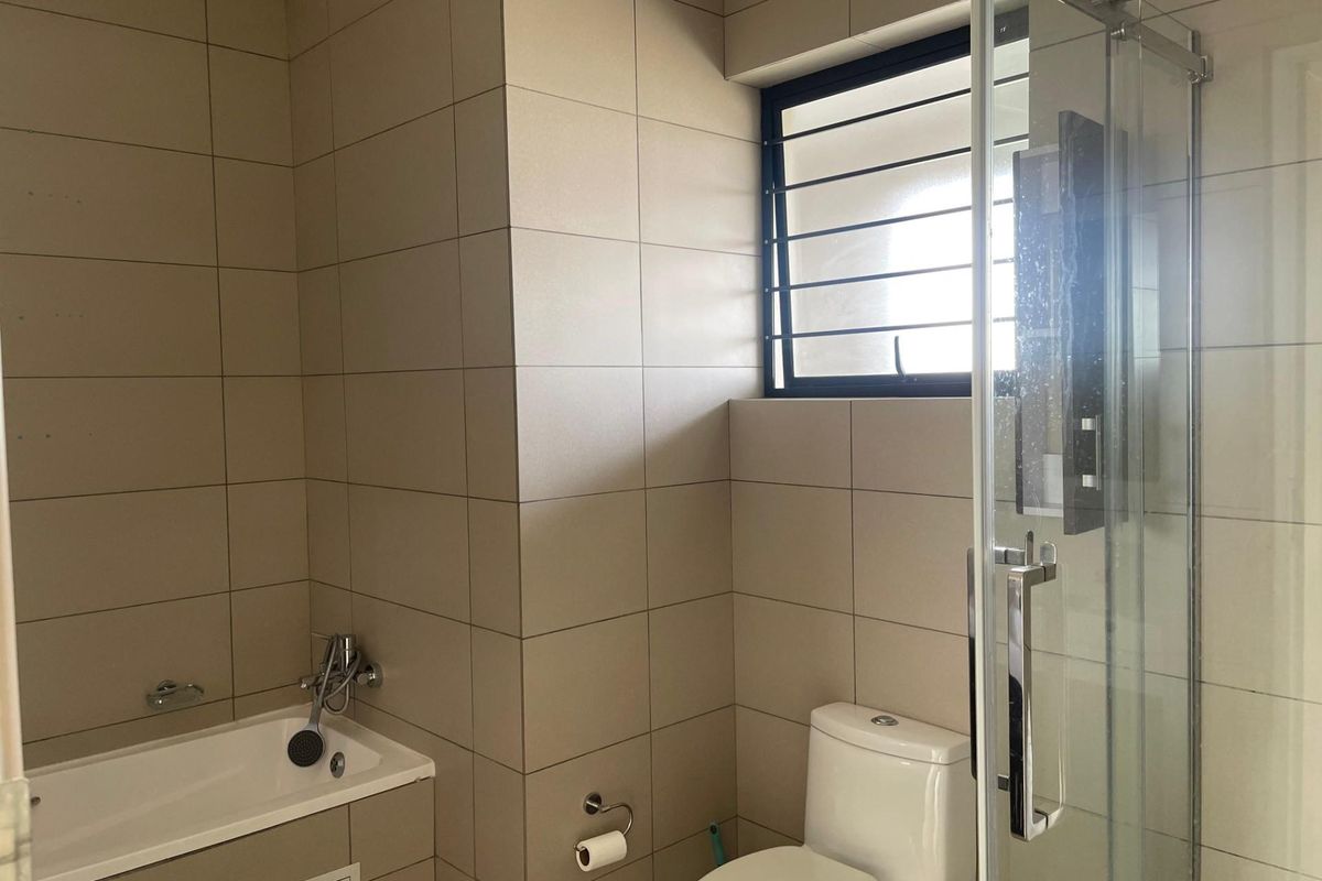 A modern bathroom featuring floor-to-ceiling neutral tiling, a built-in bathtub with shower mixer, a separate glass-enclosed shower, and a toilet.