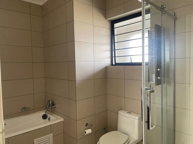 A modern bathroom featuring floor-to-ceiling neutral tiling, a built-in bathtub with shower mixer, a separate glass-enclosed shower, and a toilet.