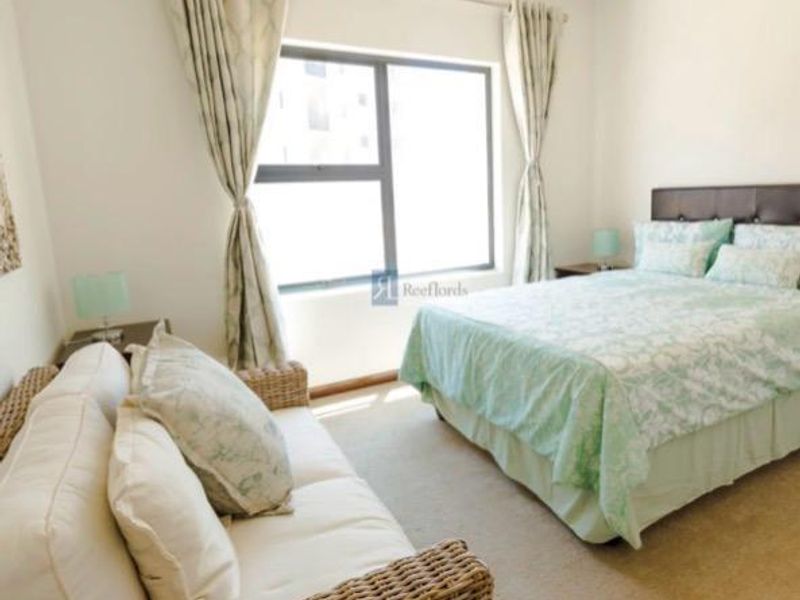 A bedroom featuring neutral carpeting, a large window with curtains, and space for a bed and seating area.