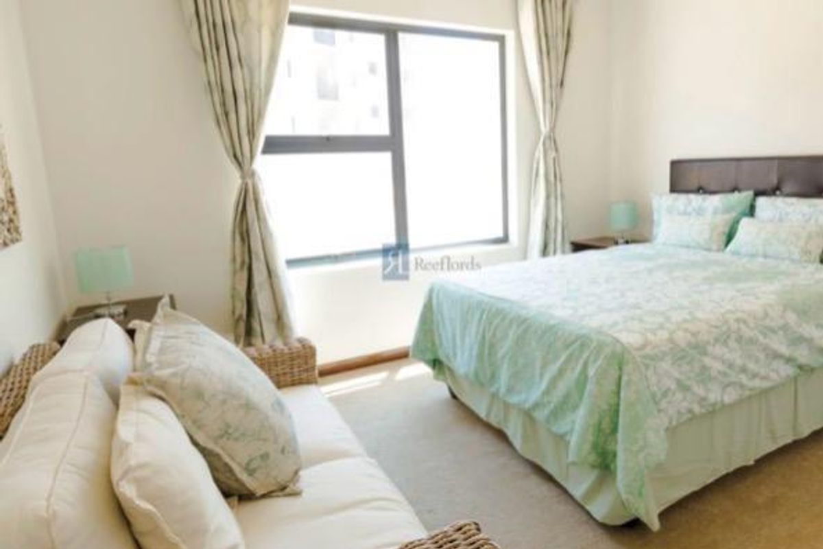 A bedroom featuring neutral carpeting, a large window with curtains, and space for a bed and seating area.
