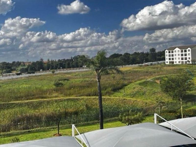 A scenic elevated view overlooking a landscaped estate with green fields, a perimeter fence, and nearby residential apartment buildings.