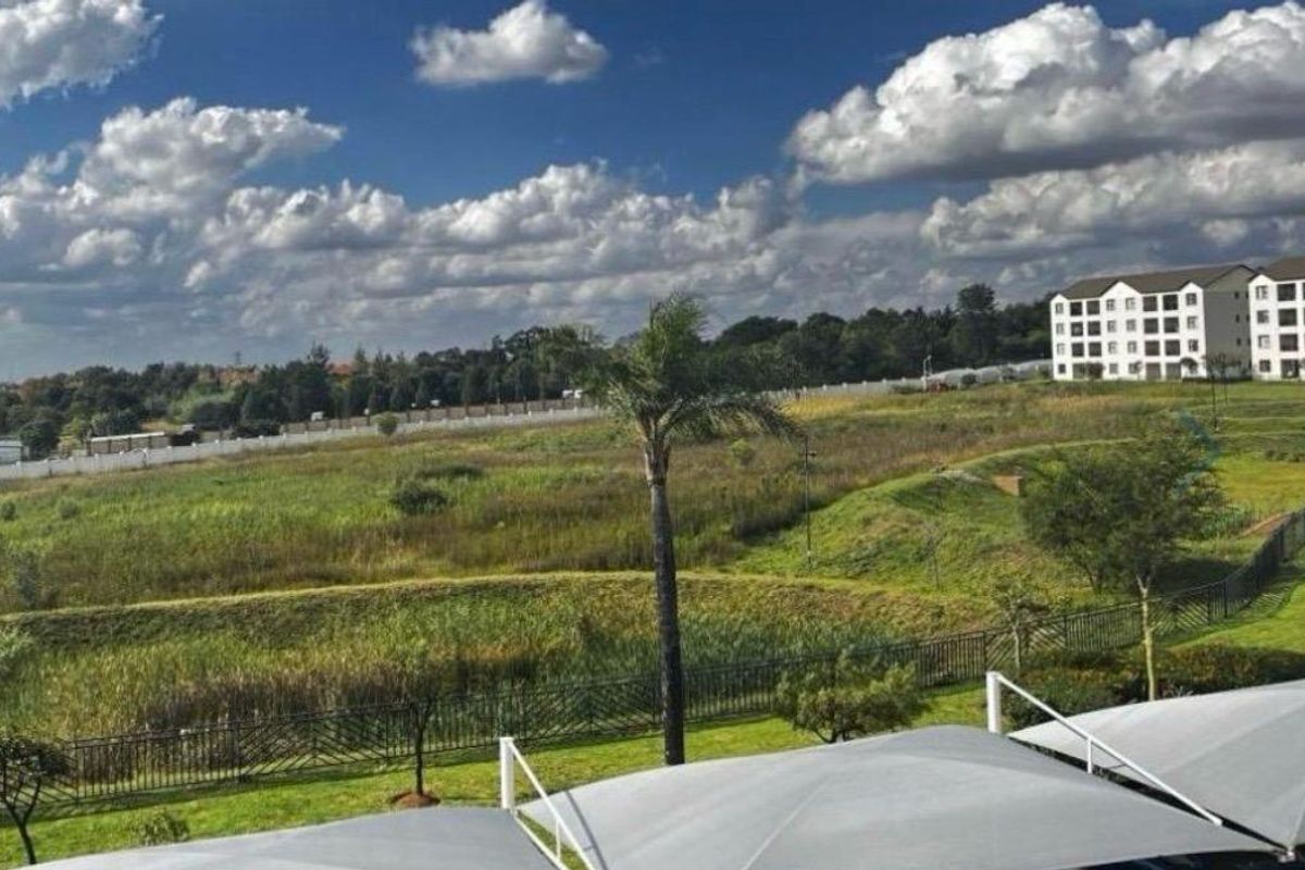 A scenic elevated view overlooking a landscaped estate with green fields, a perimeter fence, and nearby residential apartment buildings.