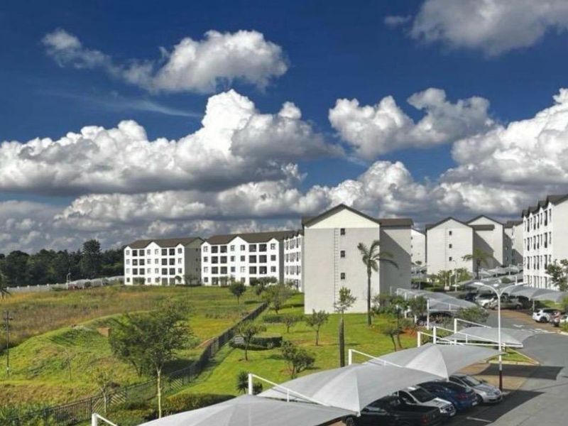 An elevated view of a modern apartment complex featuring landscaped grounds, paved parking areas with shade cloth carports, and multi-story residential buildings.