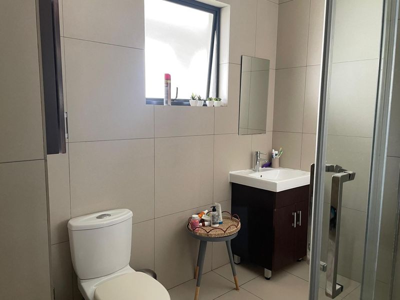 A modern bathroom featuring large-format wall tiles, a vanity with a basin, a toilet, and a glass-enclosed shower.