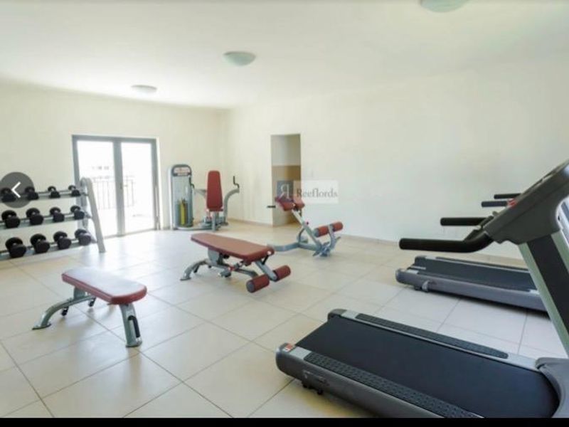 A well-lit communal gym facility featuring tiled flooring and access to an outdoor balcony area.