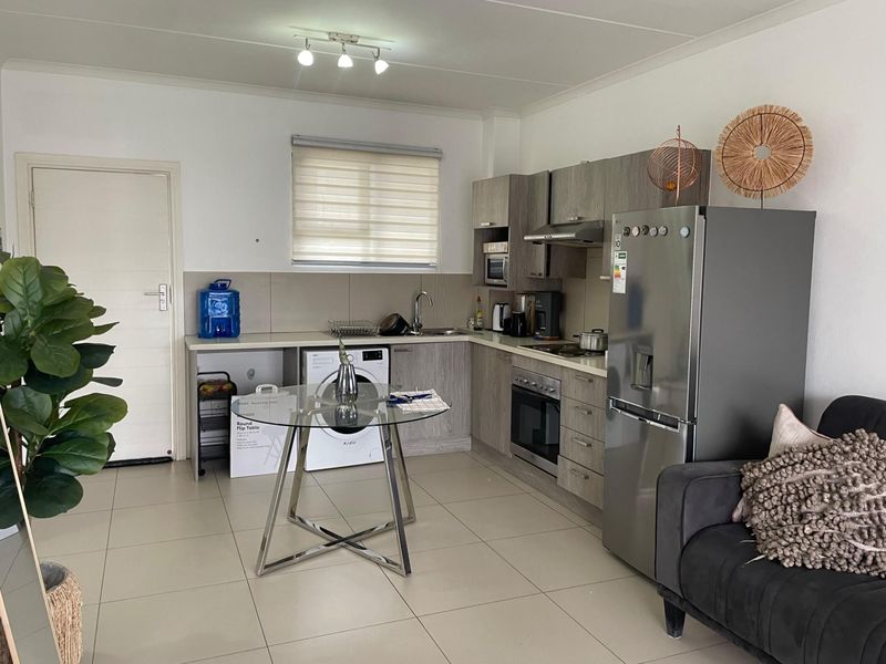 Open-plan kitchen featuring modern grey cabinetry, built-in oven, hob, extractor fan, and integrated laundry plumbing, set against neutral tiled flooring.