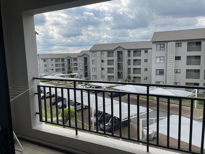 A view from a balcony overlooking the apartment complex parking area with shade-net carports.