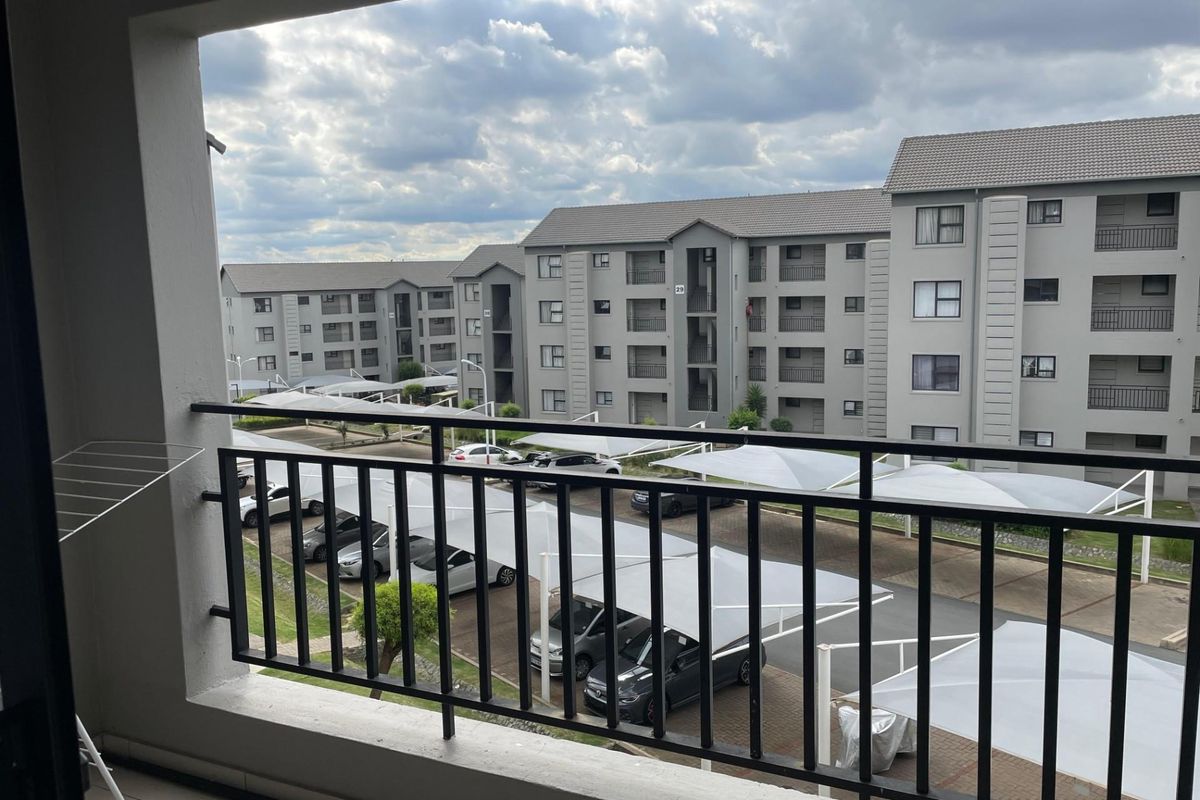 A view from a balcony overlooking the apartment complex parking area with shade-net carports.