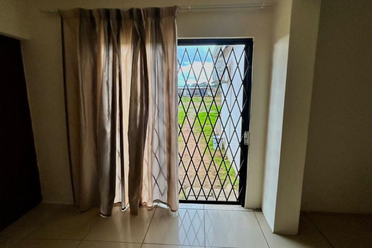 Interior view of a living area featuring large floor tiles and a security gate leading to the rear garden.