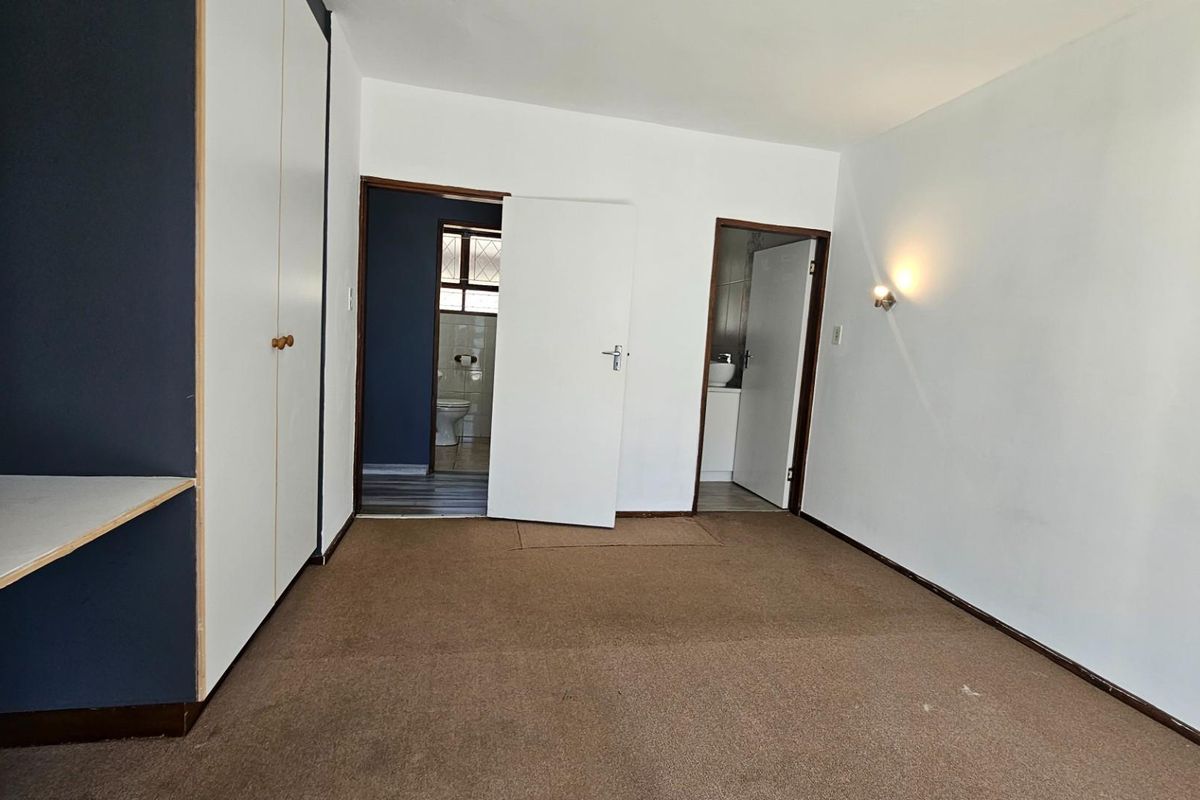 A spacious bedroom featuring built-in cupboards, a desk area, and direct access to an en-suite bathroom.