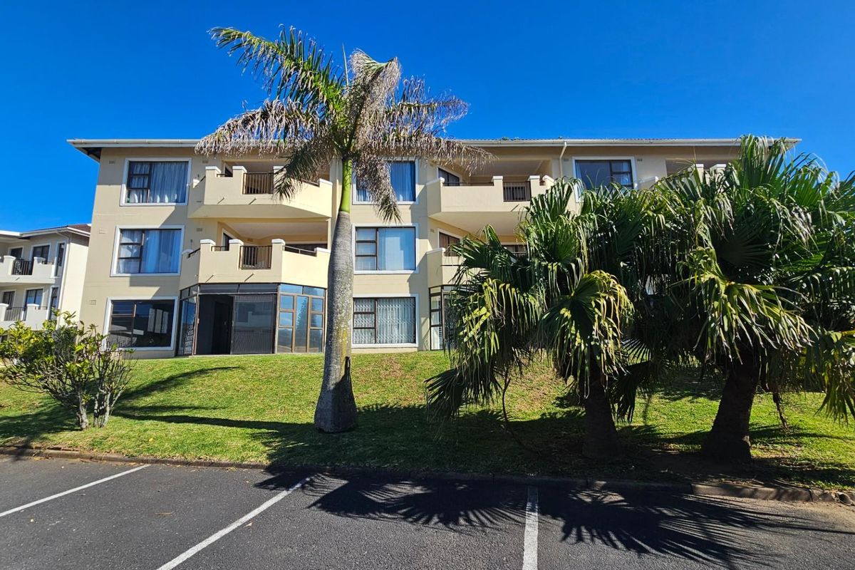 Exterior view of a multi-story apartment complex featuring balconies, large windows, and landscaped garden areas with paved parking in the foreground.