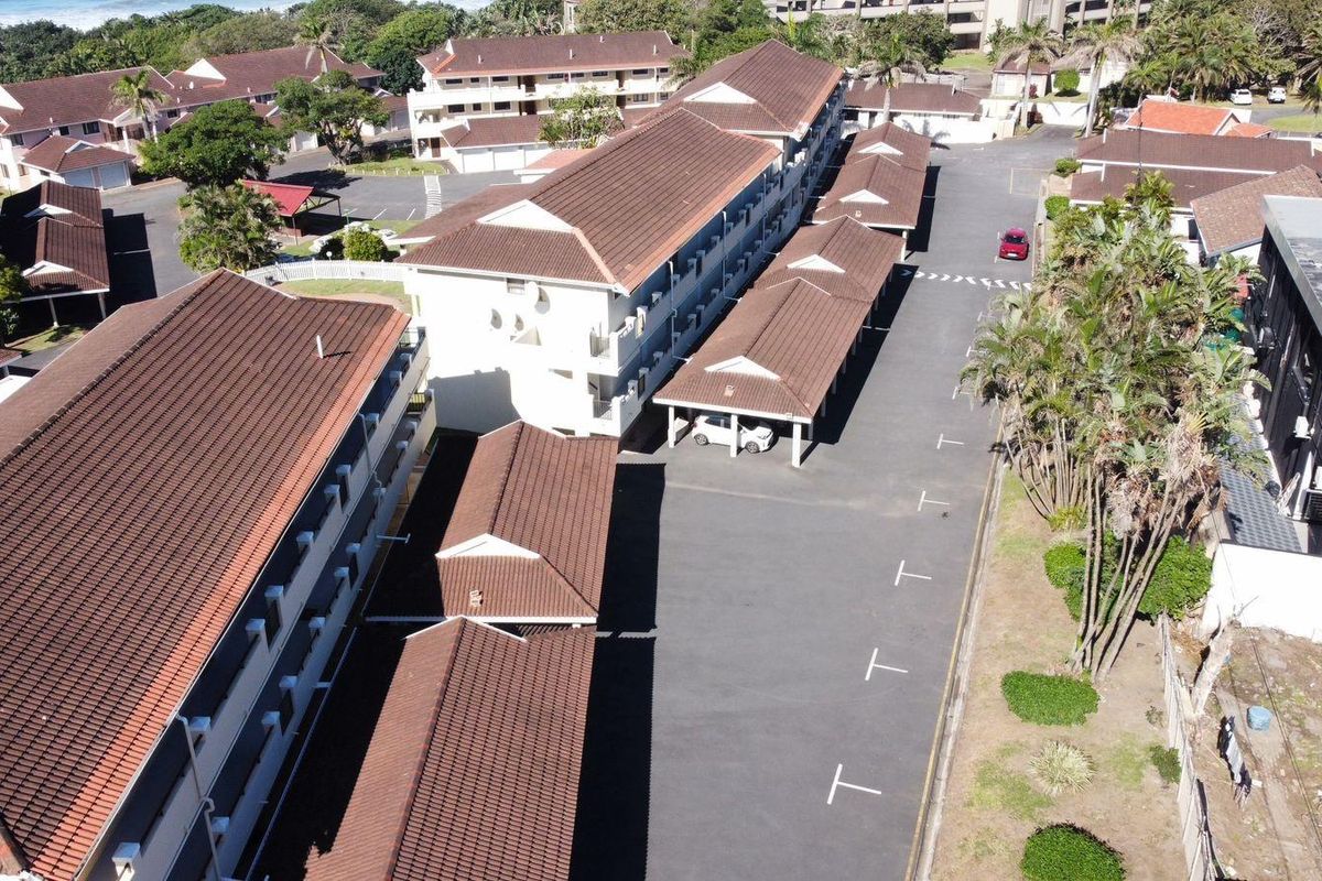 Aerial view of the apartment complex featuring multiple residential blocks, tiled roofs, covered parking bays, and surrounding landscaped grounds.