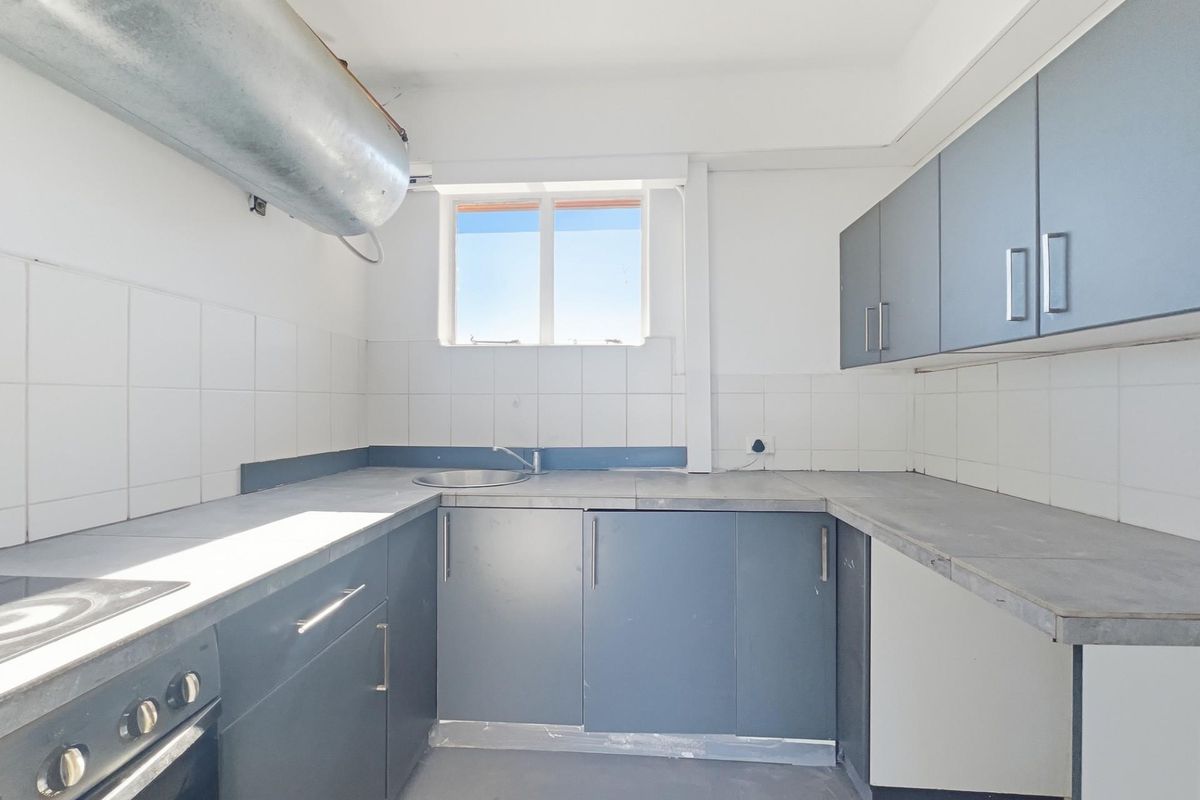 A compact kitchen featuring grey cabinetry, a built-in oven and hob, stainless steel sink, and tiled splashbacks with exposed ventilation ducting.