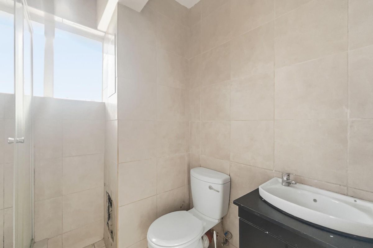 A compact bathroom featuring neutral wall tiles, a vanity basin, and a toilet, currently requiring minor repairs to the wall tiling.
