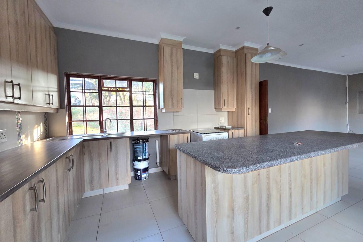 Spacious kitchen featuring light wood-look cabinetry, a large central island with stone-look countertop, tiled flooring, and a window overlooking the exterior.