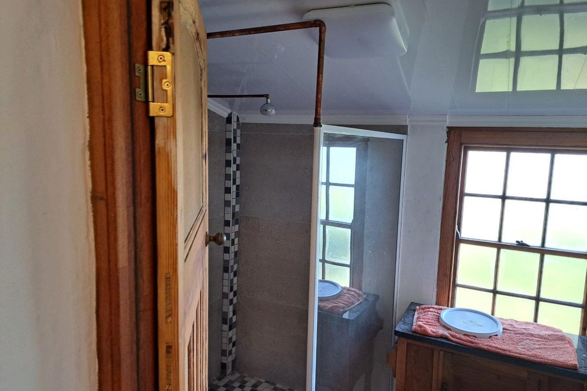A bathroom featuring a shower enclosure with tiled accents, a wooden vanity, and traditional sash windows.