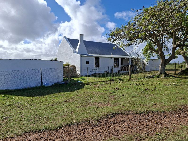 A view of the rear exterior of a traditional white farmhouse with a pitched metal roof, set within a rural landscape.